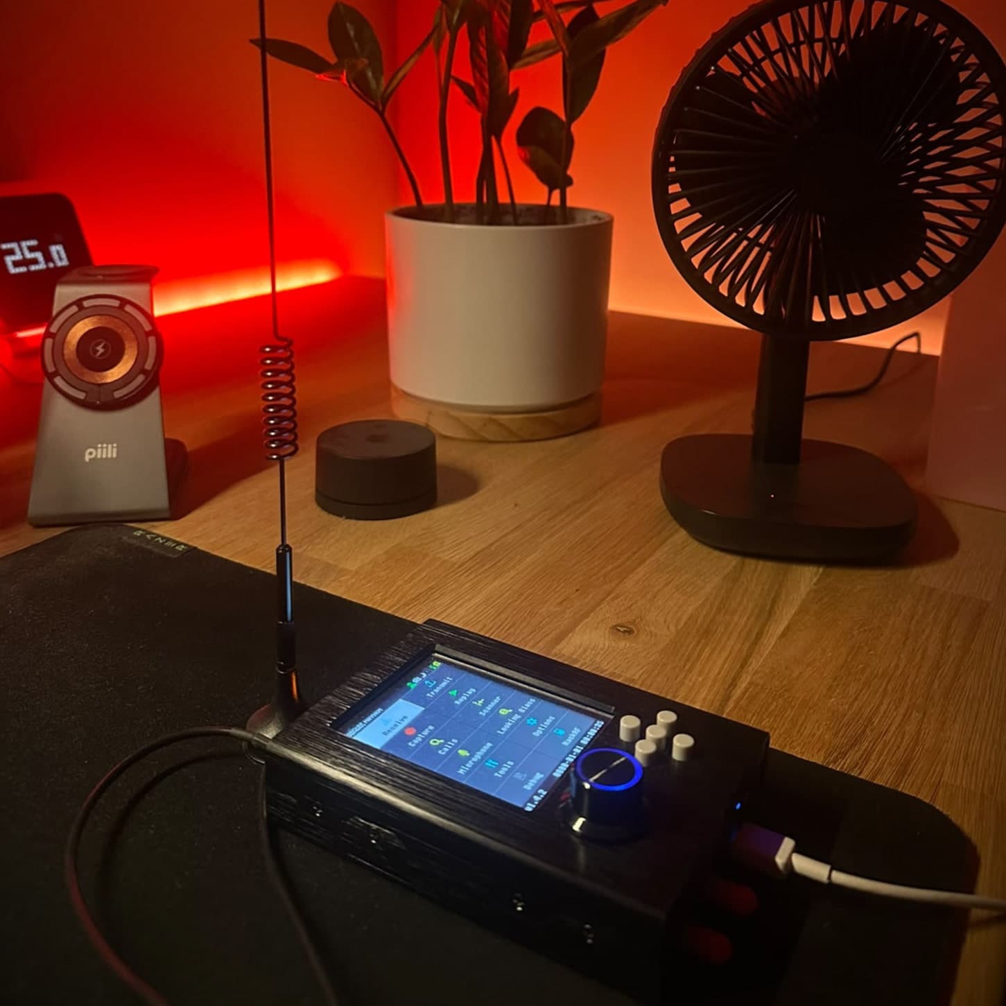A telescopic whip with a loading coil standing on a desk lit red, and below it a HackRF One in a PortaPack case showing its idle menu, with a USB cable running out of the side